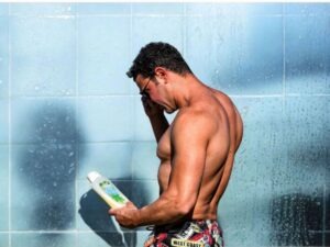Man in the shower looking at a bottle.