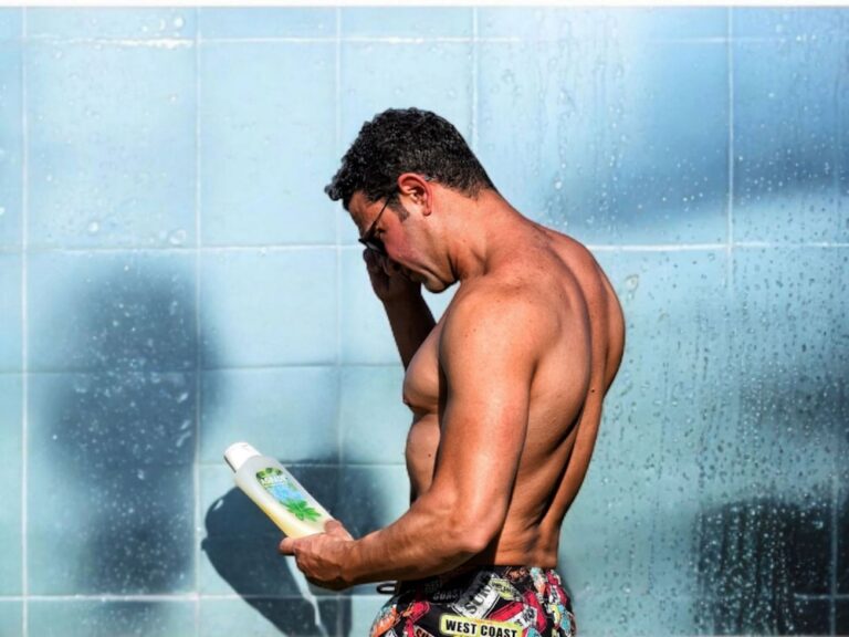 Man in the shower looking at a bottle.