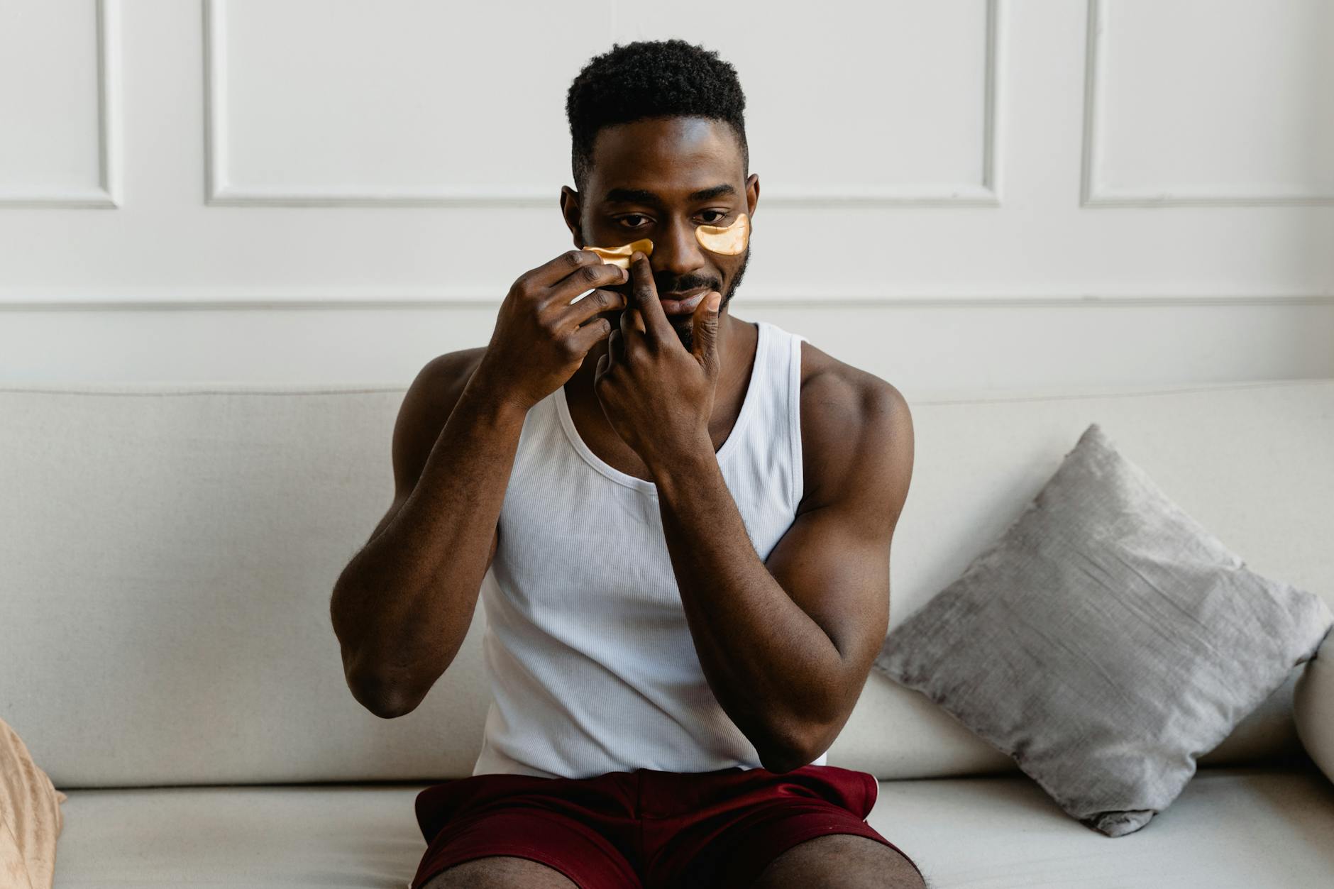 a man in white tank top putting under eye masks