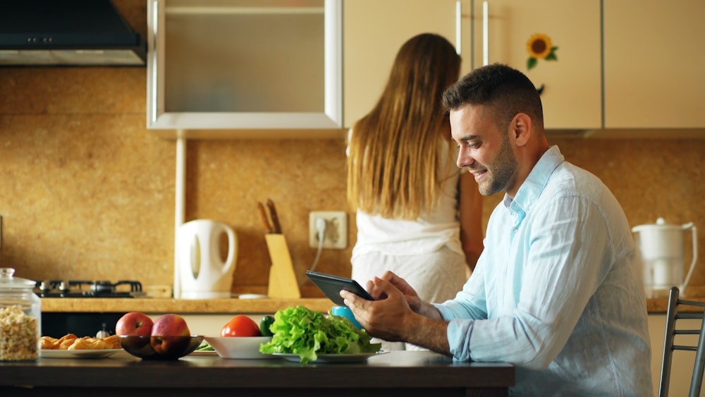 Home 6 Man using tablet in kitchen while woman stands behind him.
