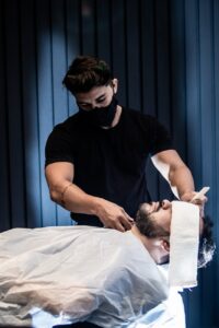 a man in black crew neck t shirt wearing a mask grooming a man s beard