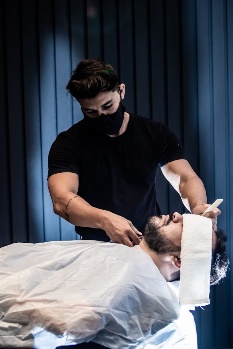 a man in black crew neck t shirt wearing a mask grooming a man s beard